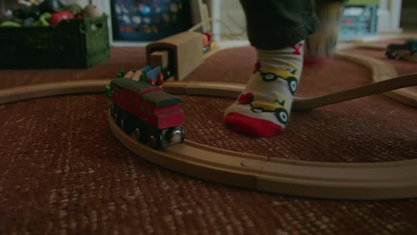 The child steps over the toy train tracks