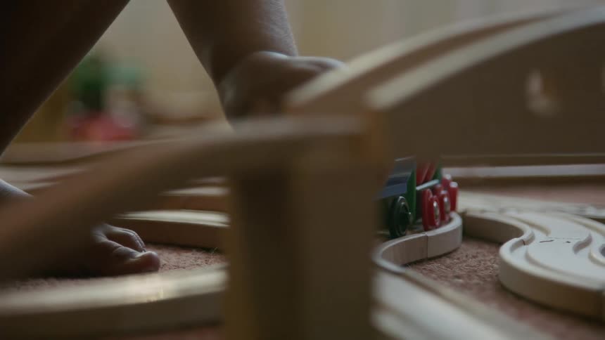 A childs feet are seen walking around a wooden train set on a floor