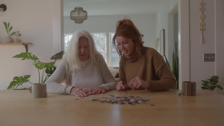 Happy grandmother and granddaughter sorting a puzzle on dining table