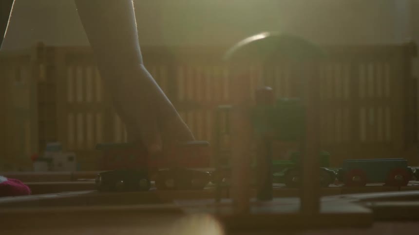 A boys hand pushes toy trains on a wooden track across a floor