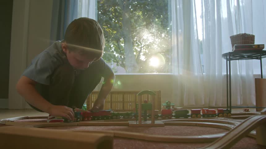 The boy is playing with his toy trainset and rolling the trains on the track