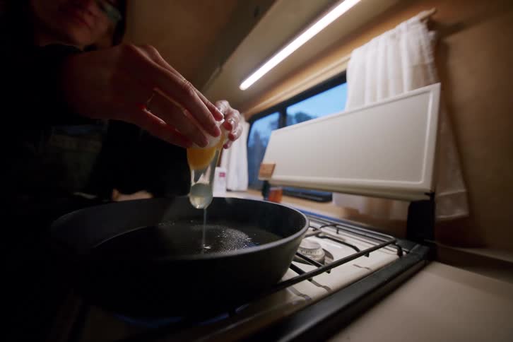 A person cracks an egg into a frying pan on a stovetop