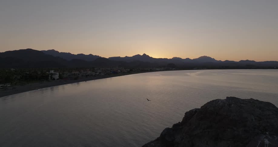 Coastal landscape at dusk with mountains in the background seaside village and golden sky reflection on calm waters