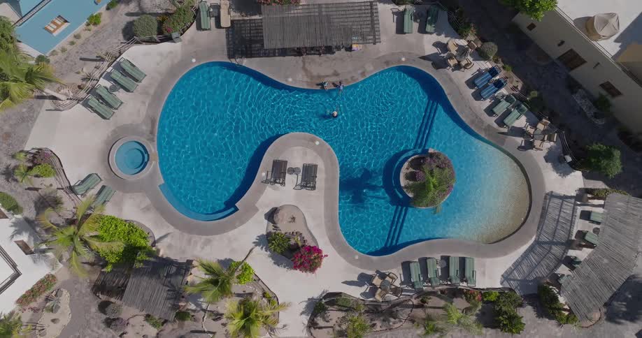 An aerial view shows three person on in a swimming pool on a hotel setting