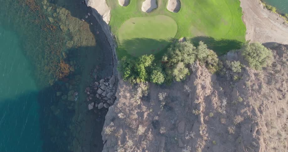Golf course seen from above next to a rocky area and a lake