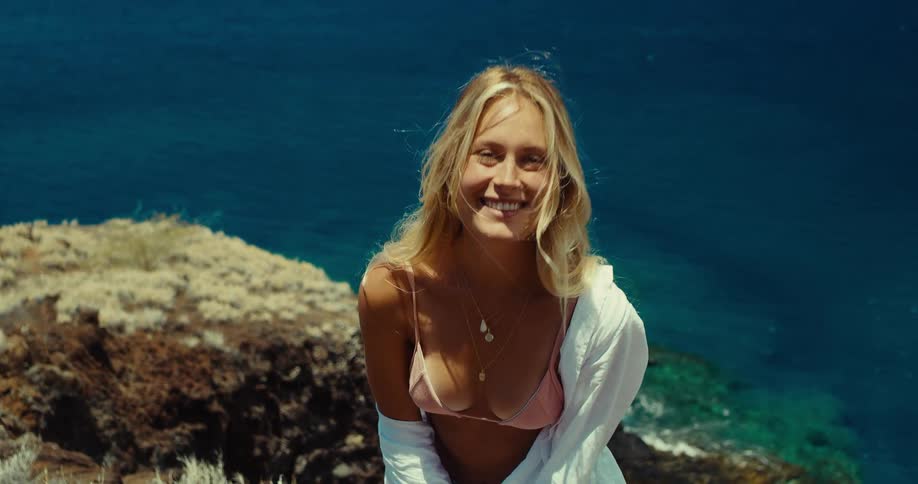 A young woman stands on a cliff and walks toward the camera laughing