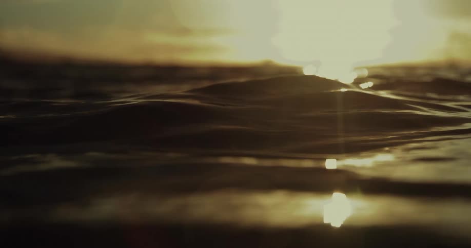Small passing wind waves reflect the sun shining from the red horizon
