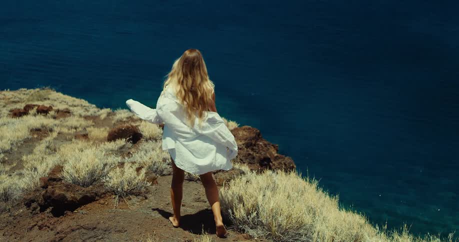 A young woman walking towards the edge of a cliff outdoors during daytime