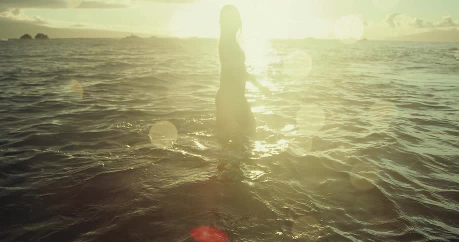 A woman walks in the water on a beach at sunset