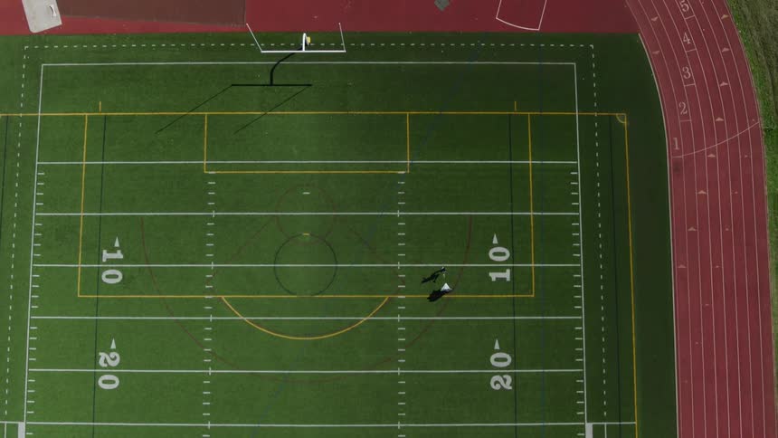 An athlete does resistance training while running with a parachute along the hash marks of a high school football field