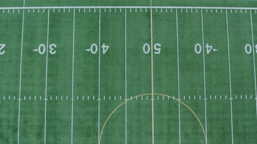 Birds eye traverse over half of the green turf of a hybrid football and soccer field