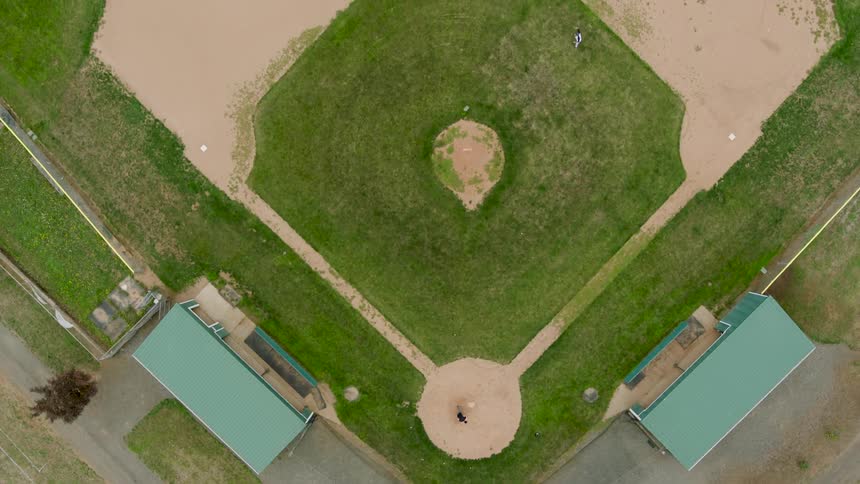 Top down view over a community baseball field with a batter hitting balls to a single outfielder between first and second base