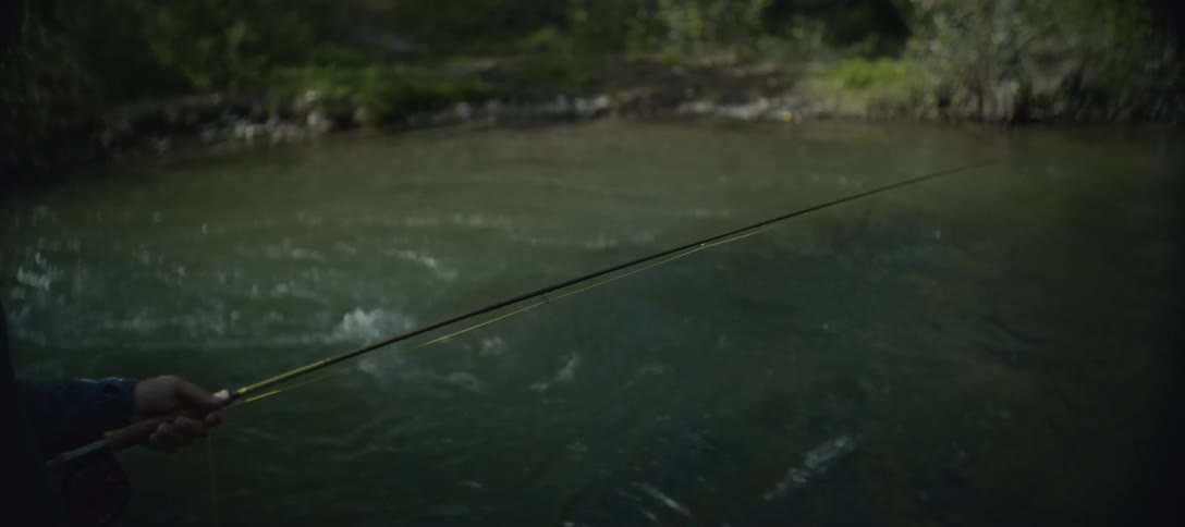 A person is fly fishing with a rod and reel on a murky river the person casts their line into the water