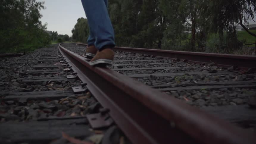 Someone balancing on, and walking along, railroad tracks in a rural area