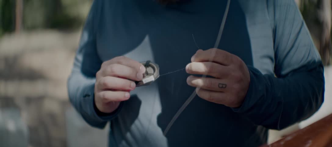 A closeup shot shows a persons hands pulling a fishing line they are winding the line around a spool