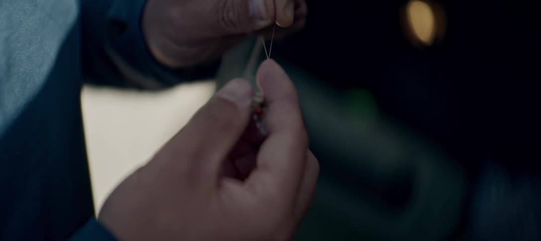 A persons hands are shown up close tying a fishing lure onto a fishing line