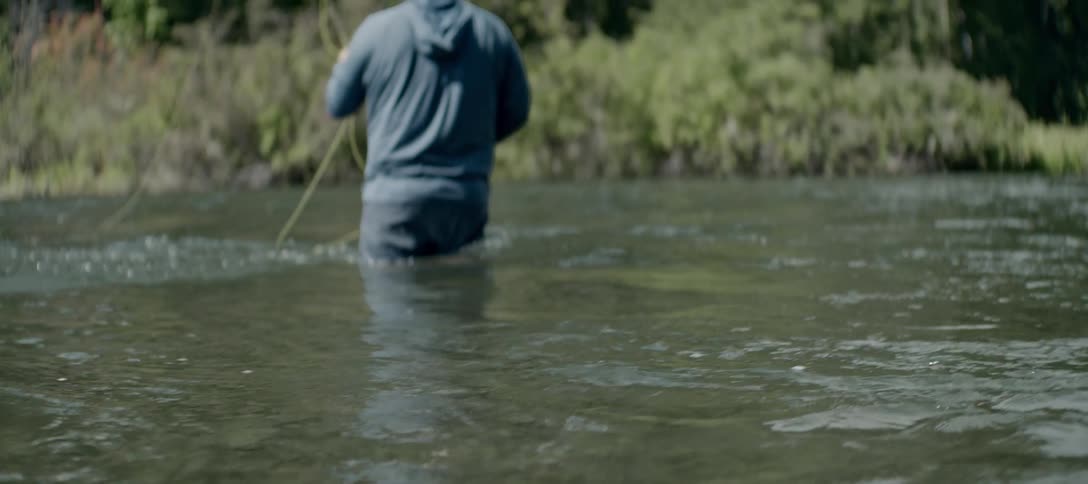 Fisherman fly fishing in a shallow river surrounded by vegetation