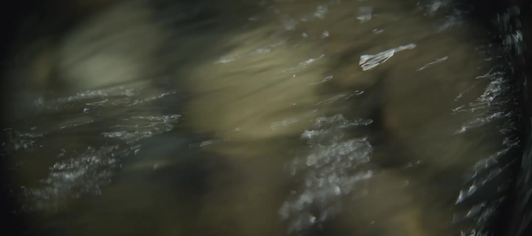 Flowing water reflects the sunlight while passing over the pebbles in a stream