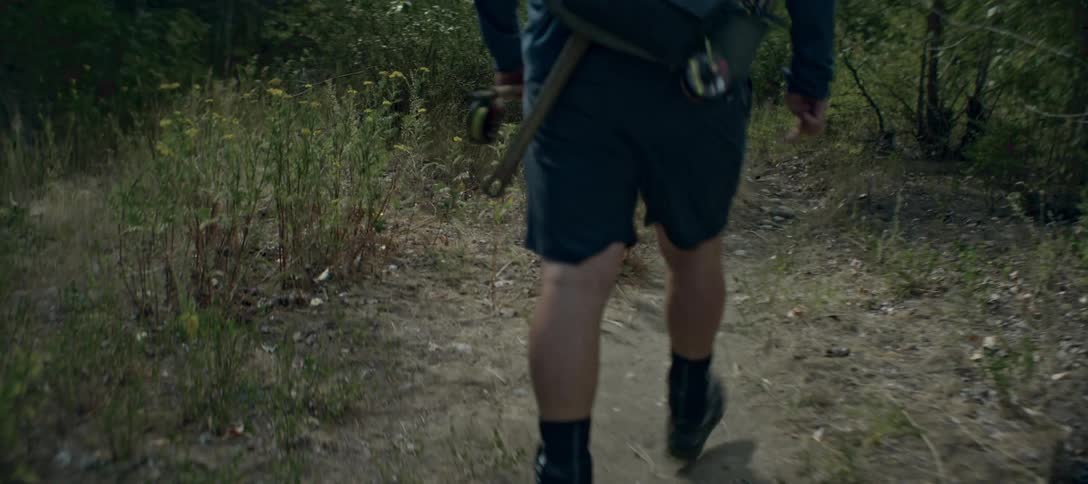 A hiker carrying a fishing rod and gear walks along a forest trail