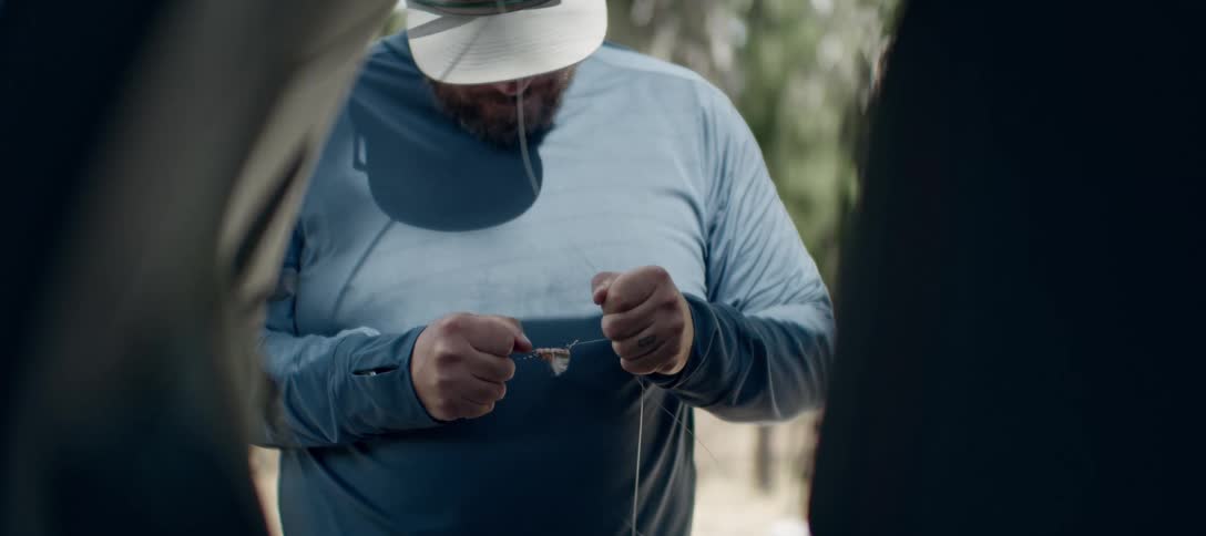 Man attaches a lure to fishing line while standing near a tent