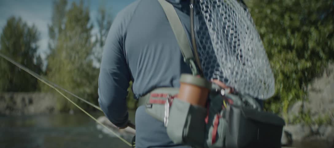 A man carrying fishing gear walking throuhg a river