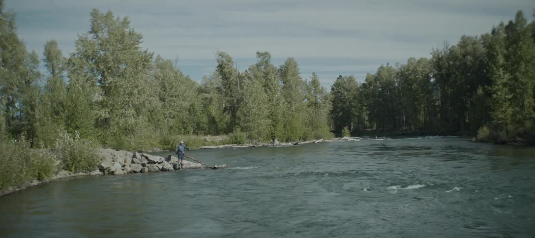 The man is fly fishing on the river bank