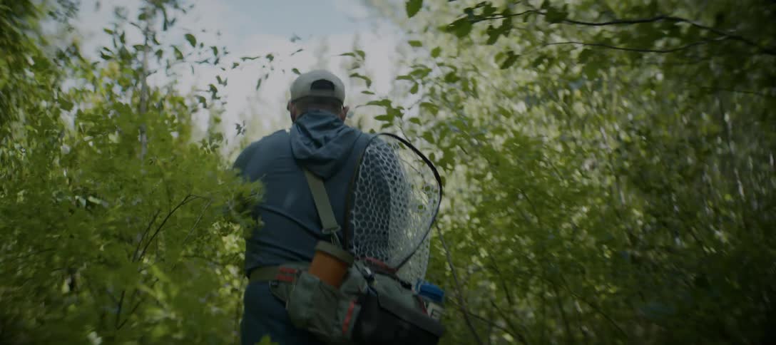 The man is walking through the brush to go fish