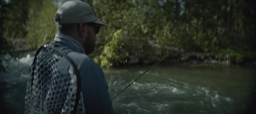 A man is fishing while standing in a river in a sunny day