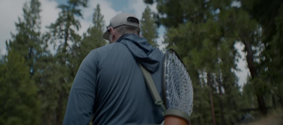 A man walks carrying fishing equipment along a forest trail