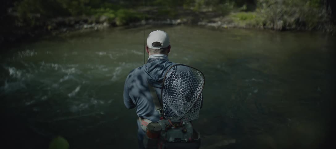 A man fly fishes in a shallow river surrounded by trees
