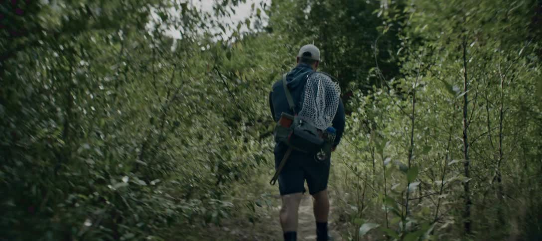 Man with a fishing net walks along a trail surrounded by dense vegetation