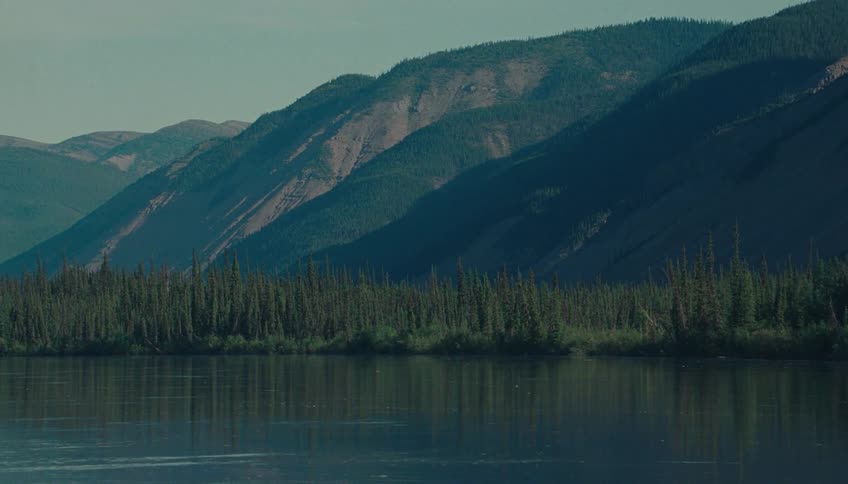 Water flows across a lake with a forested shore and nearby mountains