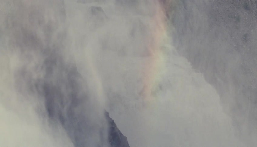Water falls down a rock formation in a continuous stream and a rainbow forms in the mist