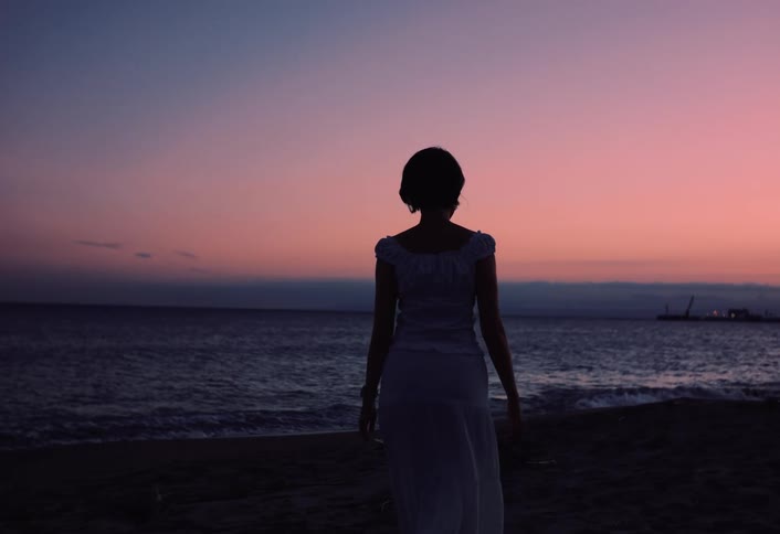 Silhouette of a woman in a dress walking towards the beach shoreline at dusk