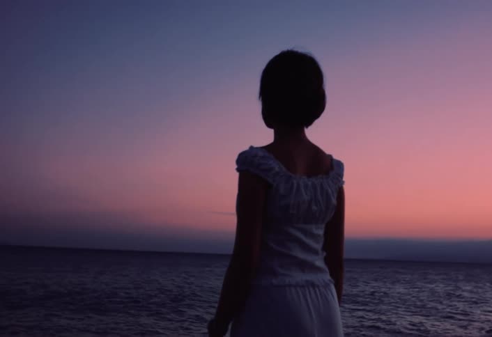 A woman standing and overlooking the ocean at sunset