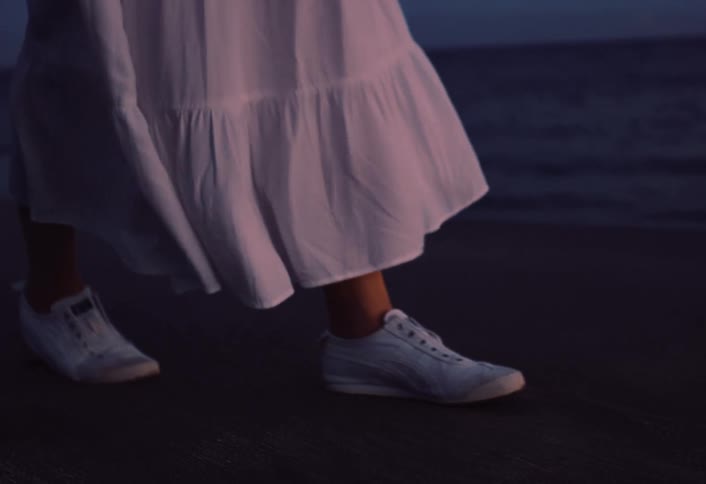 A woman walks on the shoreline the persons feet and legs are shown as they move across the sand