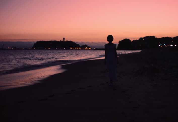 The woman is strolling on the beach at sunrise