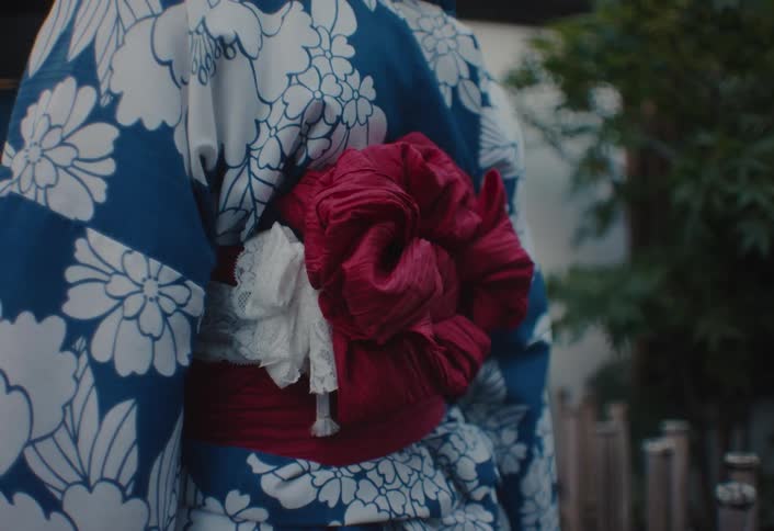 A person wearing a traditional blue and white floral kimono with a vibrant red obi sash stands outdoors