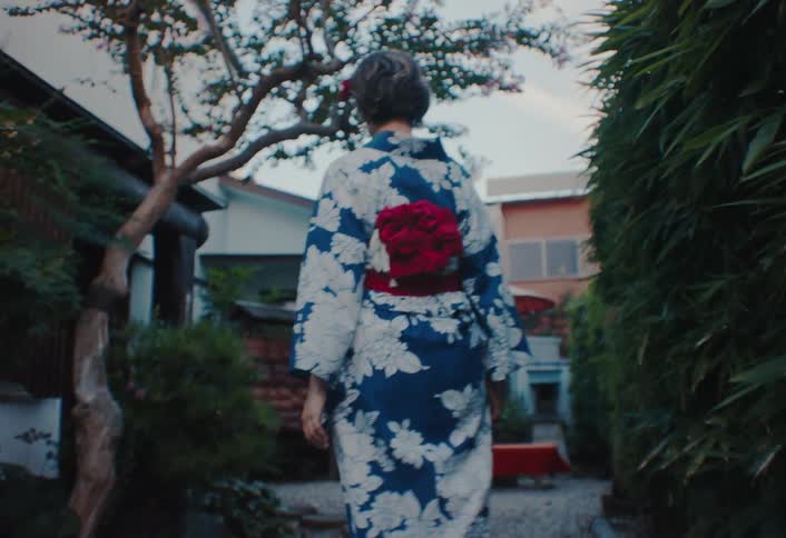 Woman in yukata walks through a traditional garden framed by bamboo and japanese architecture