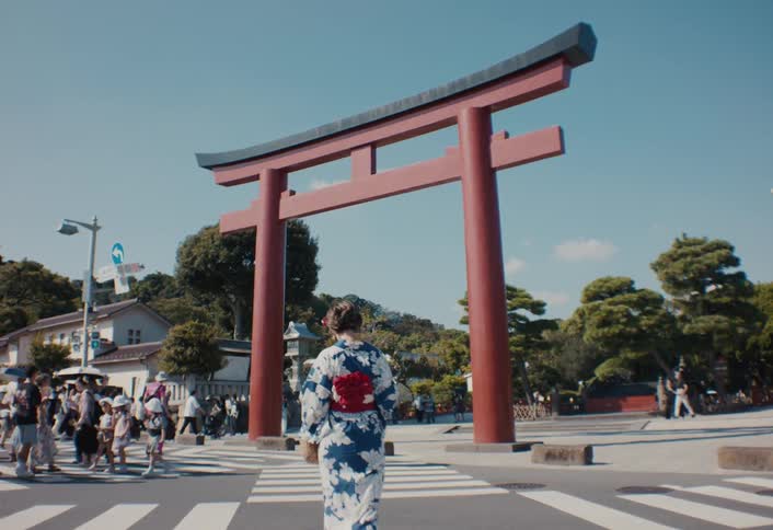Families and other people cross a street near a torii gate on a cloudy summer day