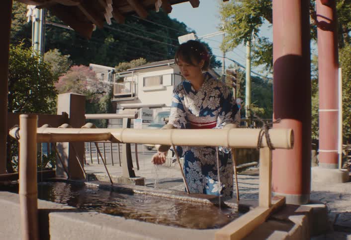 A young asian woman uses a utensil to collect water from a reservoir outdoors during daytime and rinses her hands with it