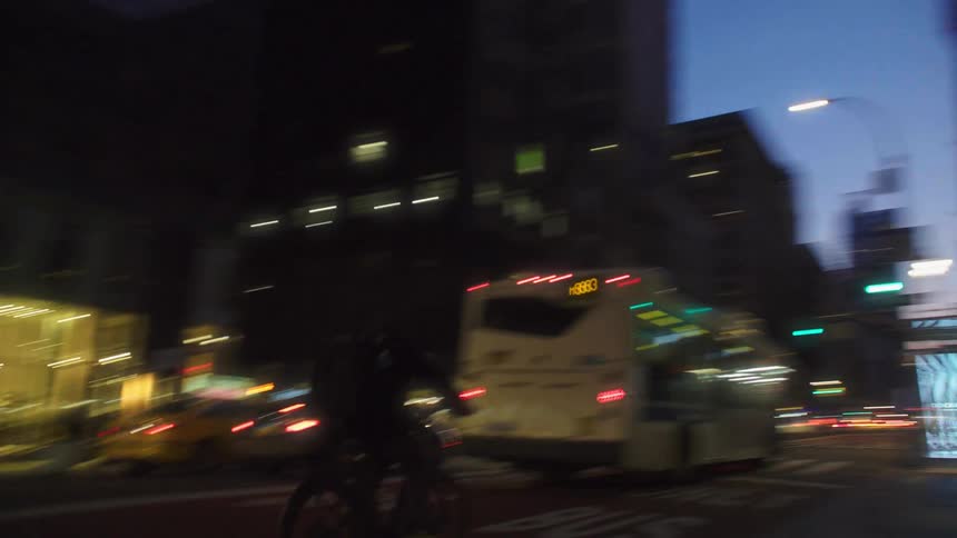 A busy city street at night with cars buses and cyclists moving past brightly lit buildings
