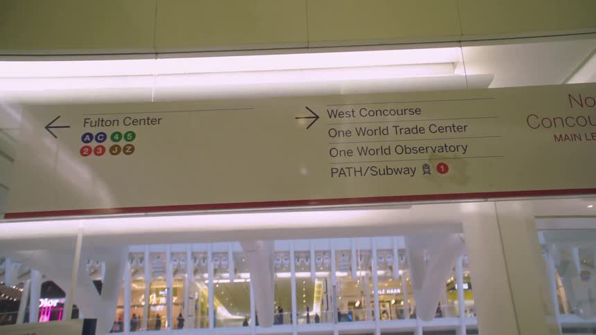 A camera moves through a busy train station with signs and advertisements
