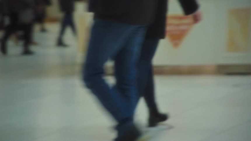 People walk side by side in a busy indoor setting with partial signage in the background