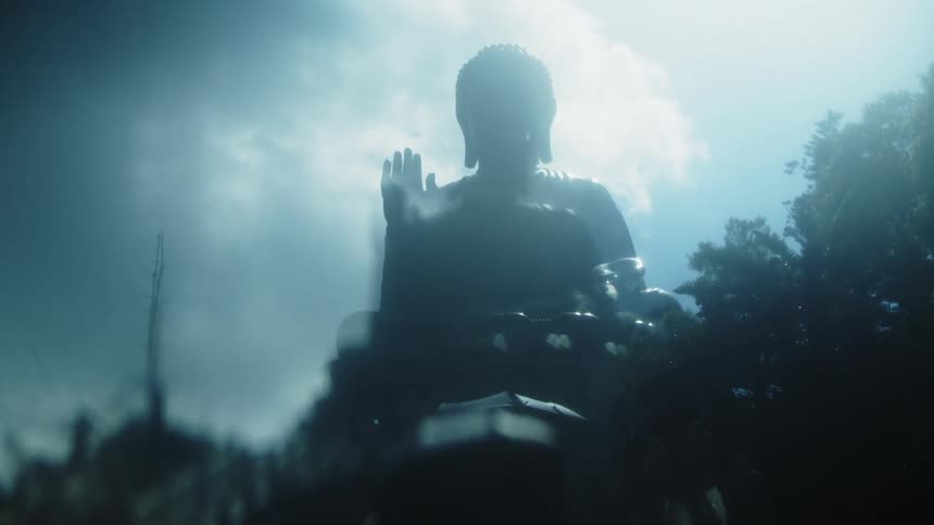 A large silhouetted statue of a seated figure with one hand raised positioned against a background of a cloudy sky