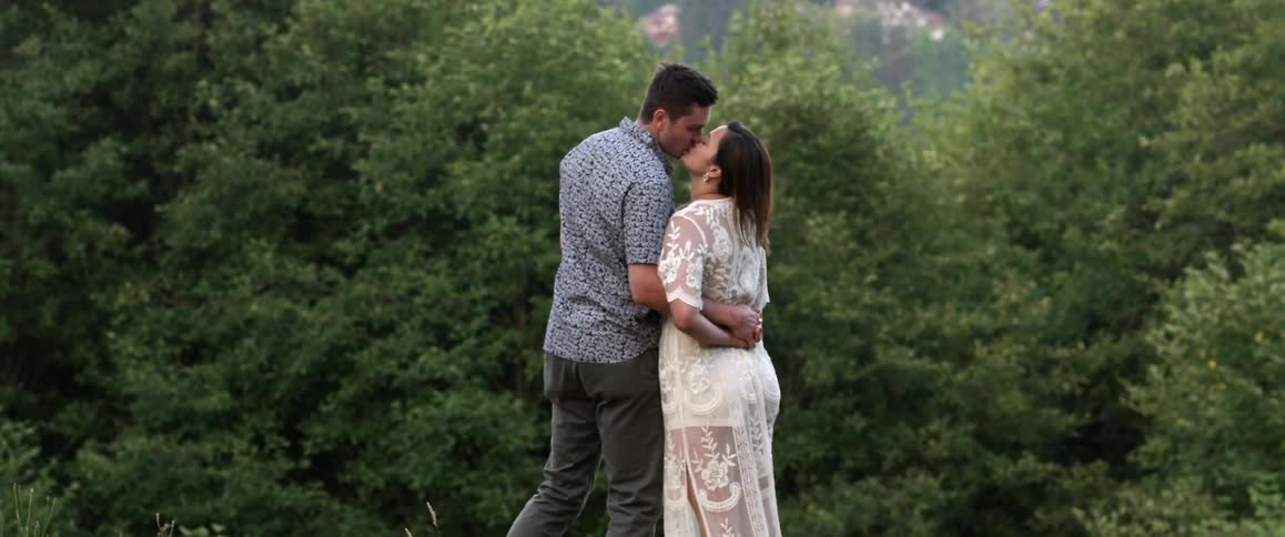 A couple kiss in front of the woods