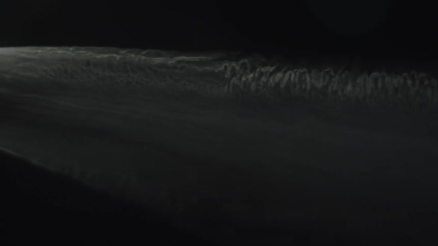 White foam spreads in a sinuous line across the dark water surface