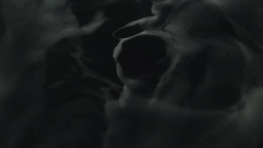 A black and white abstract video shows thick textured smoke swirling and contracting to reveal a dark empty space in the center