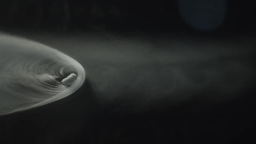A smoky swirl drifts through dark space in motion