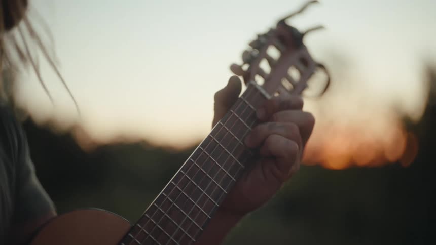 A person strums an acoustic guitar at sunset